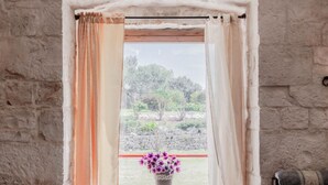 A window with curtains, a stone wall, and a view of trees and a stone wall outside. - Masseria Carbonico delle Lamie - Ginestra by Rentbeat (Martina Franca)
