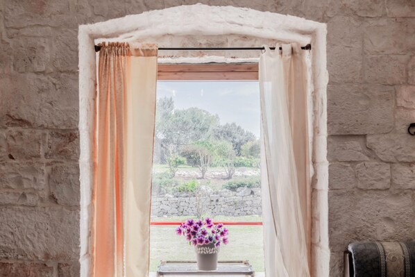 Una ventana con cortinas, una pared de piedra y vistas a árboles y otra pared de piedra.