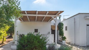 A white building with a wooden pergola, a small window, and a door.