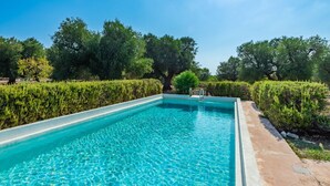A rectangular swimming pool with clear blue water, surrounded by neatly trimmed hedges and trees.