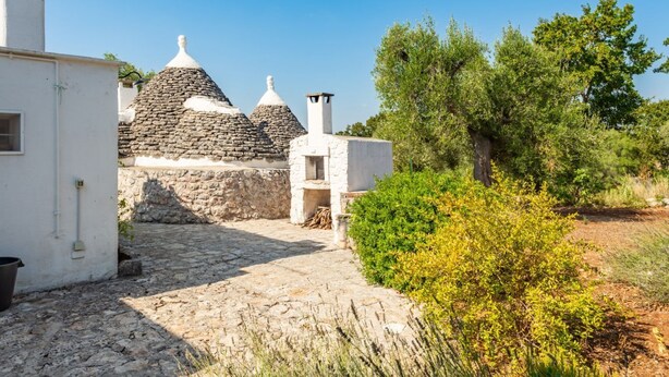 A stone pathway leading to traditional stone-roofed buildings, surrounded by greenery.