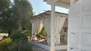 A covered outdoor seating area with a pergola, white curtains, and a white door.