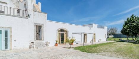 A white building with a stone patio, a covered outdoor seating area, and a small garden.