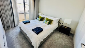 Habitación de hotel con una cama grande, una mesita de noche, una lámpara y vistas al exterior.