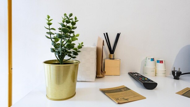 Un bureau blanc orné d’une plante en pot, avec une télécommande, un flacon de parfum, une paire de baguettes et une pile de tasses blanches.