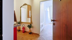 A hallway with a wooden door, a mirror, a red fire extinguisher, and a potted plant. - La Posada by Rentbeat (Civitavecchia)