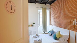 A bedroom with a bed, a desk, a chair, a window with curtains, and a brick wall. - La Posada by Rentbeat (Civitavecchia)