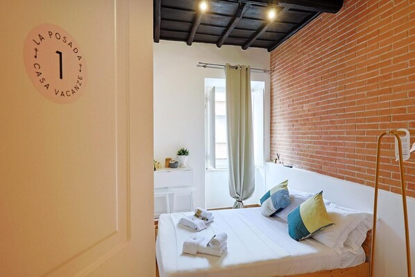 A bedroom with a bed, a desk, a chair, a window with curtains, and a brick wall. - La Posada by Rentbeat (Civitavecchia)