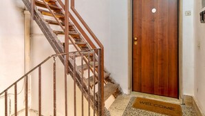 A wooden staircase with a metal railing leading to a wooden door with a 'WELCOME' mat. - La Posada by Rentbeat (Civitavecchia)