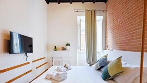 Une chambre d’hôtel avec un lit, un téléviseur à écran plat, une fenêtre avec des rideaux et un mur en briques.