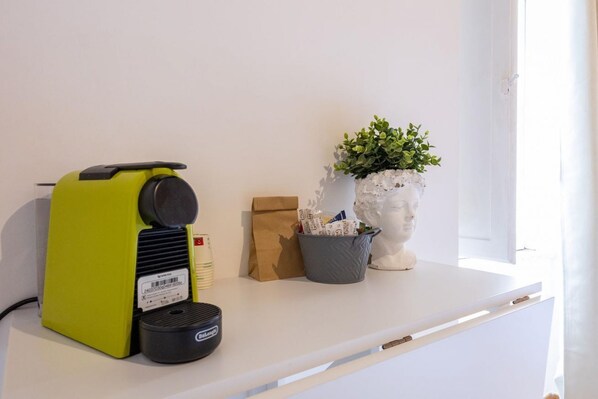 A white shelf with a green appliance, a brown paper bag, a grey container with a plant, and a white bust sculpture. - La Posada - Camera 1 by Rentbeat (Civitavecchia)