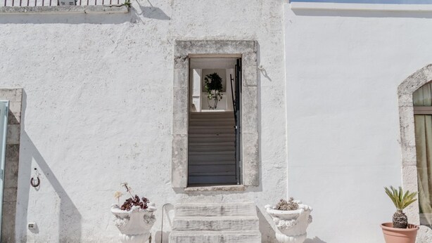 A white building with a small window, a set of stairs leading to the entrance, and two potted plants. - Masseria Carbonico delle Lamie - Suite by Rentbeat (Martina Franca)