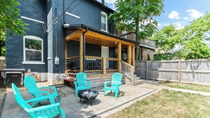 Ein Hinterhof mit einer Holzterrasse, einer überdachten Veranda und Gartenmöbeln mit Stühlen und einem Tisch.