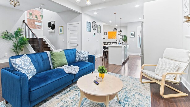Ein modernes Wohnzimmer mit einem blauen Sofa, einem Holztisch und einem weißen Sessel. Eine Treppe führt zu einer erhöhten Ebene.