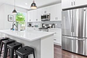 A modern kitchen with white cabinetry, stainless steel appliances, and a central island with bar stools.