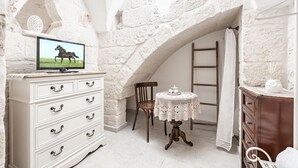 A room with a white dresser, a television displaying a horse, a small round table with a lace tablecloth, and a wooden chair. - Portici Guest House by Rentbeat (Fasano)