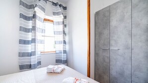 A bedroom with a bed, striped curtains, a wardrobe, and towels on the bed. - Residence Anna by Rentbeat (Villanova)
