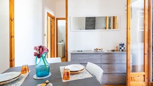 A dining area with a table set for two, a vase with flowers, and a kitchen in the background. - Residence Anna by Rentbeat (Villanova)