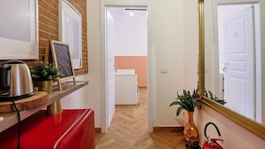 A hallway with a red bench, a kettle, a plant, a framed picture, and a mirror. - La Posada - Camera 2 by Rentbeat (Civitavecchia)