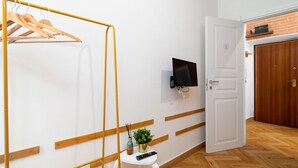 A room with a wooden hanger rack, a small white table with a remote control, a potted plant, and a television mounted on the wall. - La Posada - Camera 2 by Rentbeat (Civitavecchia)