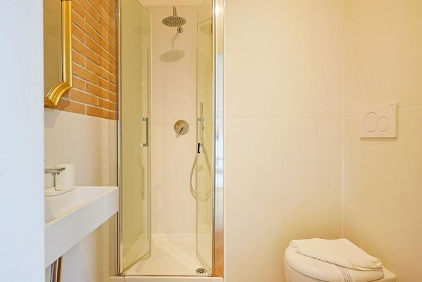 Un bany modern amb dutxa de vidre, un lavabo blanc i un vàter.