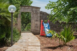 A pathway leading to a stone archway, a playground with slides, and a street lamp. - Masseria Fumarola Il Cavaliere I by Rentbeat (Ostuni)