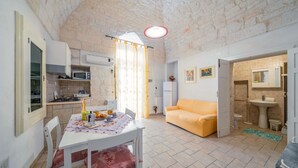 A compact kitchen with a dining area, a sofa, and a bathroom visible through an open door. - Salentina by Rentbeat (Ostuni)