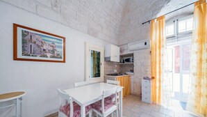A compact kitchen with a dining area, a white table, and chairs. There is a framed picture on the wall, a window with curtains, and a microwave. - Salentina by Rentbeat (Ostuni)