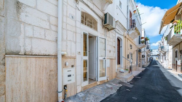 A narrow street with buildings on either side, a clear sky, and a visible door on the left. - Salentina by Rentbeat (Ostuni)
