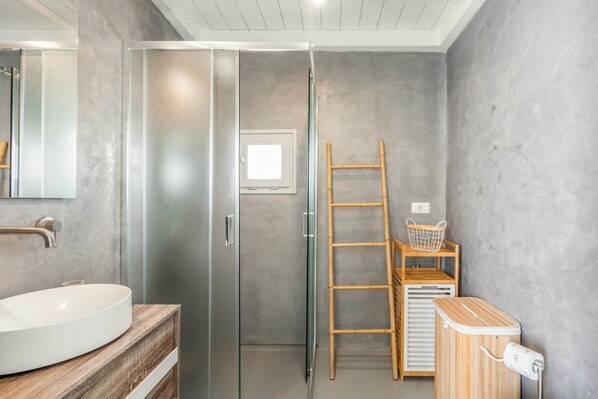 A bathroom with a glass shower door, a wooden vanity with a sink, a ladder, and a wooden shelf with a basket.