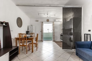 Sala de estar com área de jantar, um sofá azul, televisão e cozinha visível por uma porta aberta.