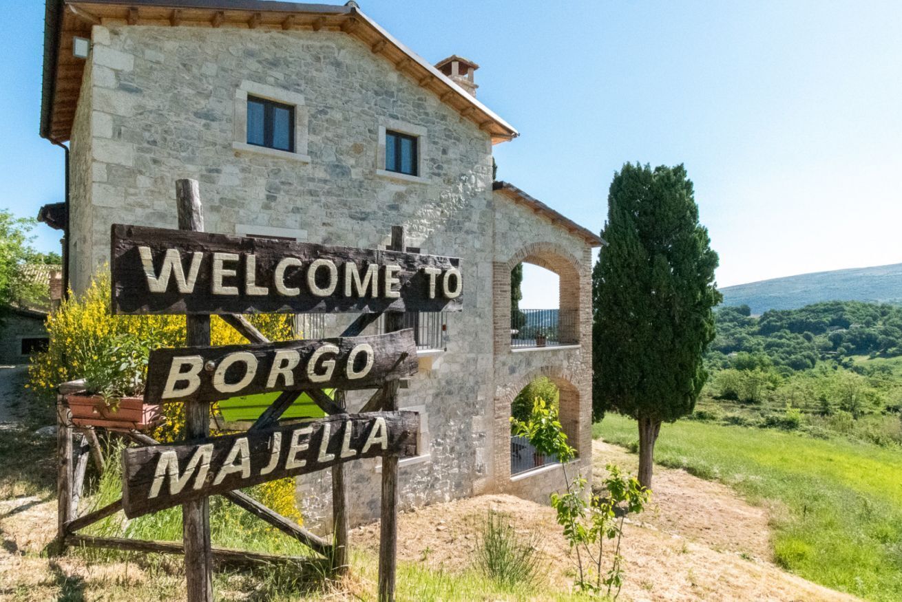 Ein Steinhaus mit einem Schild, auf dem 'WELCOME TO BORGO MAJELLA' steht, und einem rustikalen hölzernen Wegweiser.