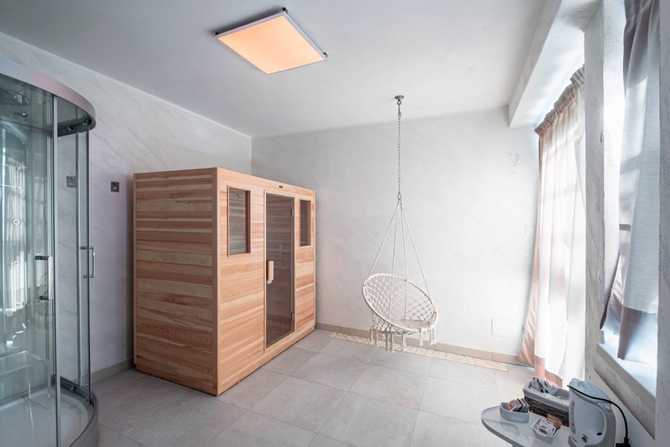 Une chambre moderne dotée d’une douche à parois de verre, d’un meuble en bois, d’un fauteuil suspendu et d’une petite table avec une station de recharge.