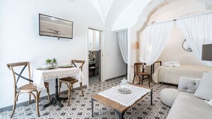 Ein Zimmer mit Esstisch, Stühlen, einer Couch, einem Bett und einem an der Wand befestigten Fernseher.