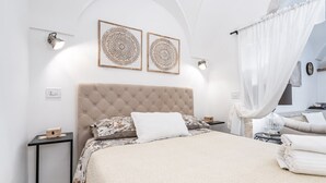 Ein ordentlich eingerichtetes Schlafzimmer mit einem gesteppten Kopfteil, einem Bett mit gemusterten Bettwäsche, zwei Wandleuchten und einem Nachttisch mit einer Lampe.