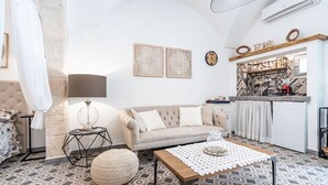 Ein Wohnzimmer mit einer Couch, einem Couchtisch, einer Lampe und einem Küchenbereich mit einer Uhr und einem Schild mit der Aufschrift 'HOME'.