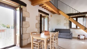 A spacious room with a wooden dining table, a grey sofa, and a staircase with wooden beams. - Nonna Francesca by Rentbeat (Abbateggio)