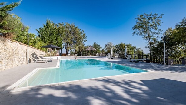 A rectangular swimming pool with a stone wall on one side and a paved deck area with lounge chairs and umbrellas. - Nonna Francesca by Rentbeat (Abbateggio)