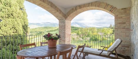 Un patio coperto con tavolo e sedie, una poltrona relax e vista su un paesaggio verde.