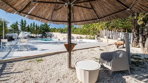 A pool area with a thatched umbrella, outdoor seating, and a gravel ground. - Nonna Francesca by Rentbeat (Abbateggio)
