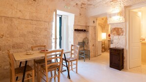 A room with a stone wall, a wooden table with chairs, a door, and a small cabinet. - Masseria Fumarola Il Cavaliere IV by Rentbeat (Ostuni)