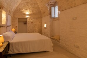 Une chambre aux murs de pierre, avec un lit, des lampes de chevet et une petite fenêtre.