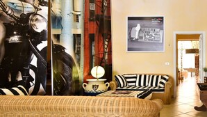 A wicker sofa, a striped pillow, a white pot with a blue design, and a framed picture on the wall.