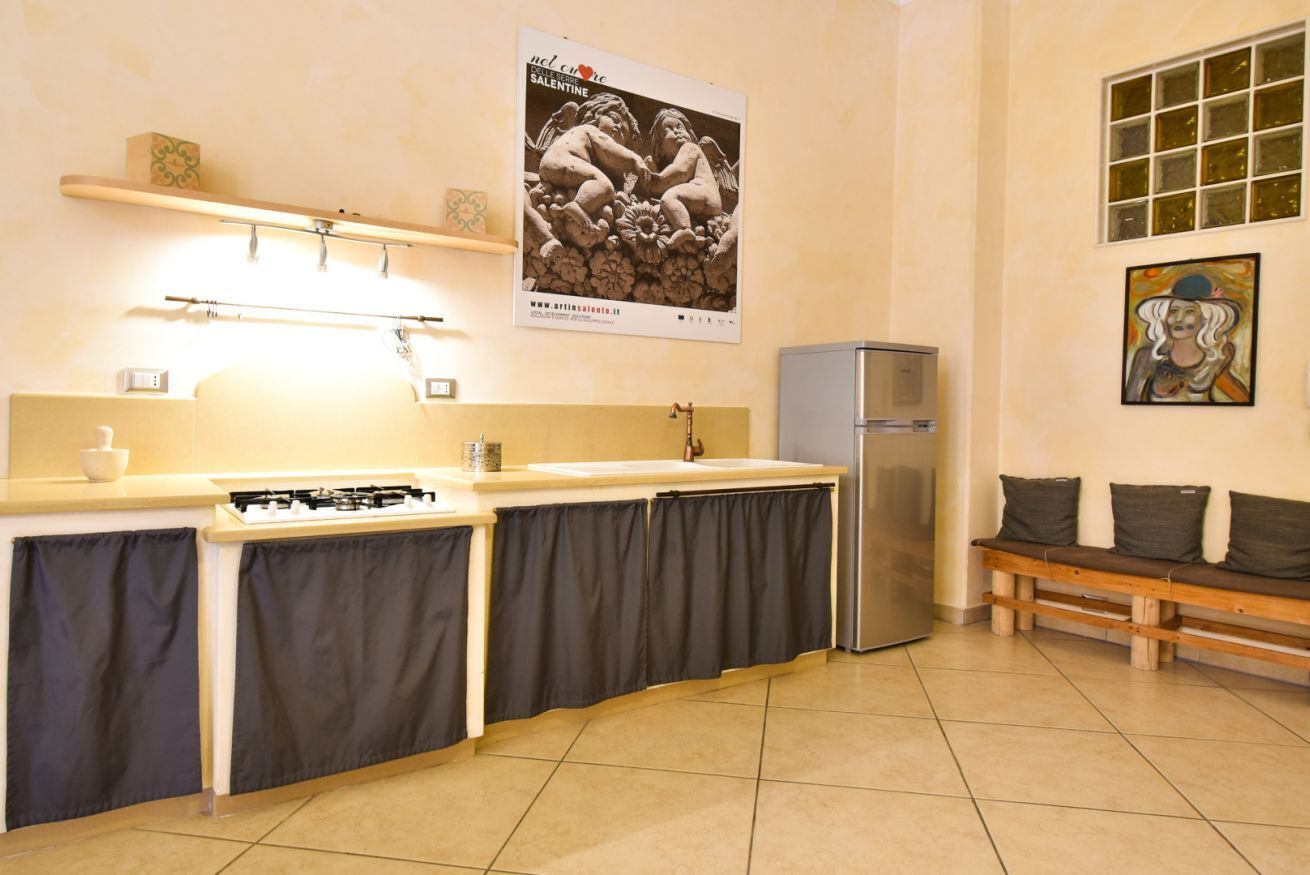 Une cuisine équipée d’une cuisinière à gaz, d’un évier et d’un réfrigérateur. On y trouve également un banc avec des coussins et un tableau accroché au mur.