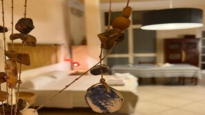 A room with a bed, a hanging decorative item, and a dining area in the background.