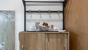 A wooden cabinet with a metal rack above it, containing various items like a basket, newspapers, and a bottle. - Street View Apartment by Rentbeat (Bari)