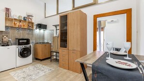 A compact kitchen with a washing machine, wooden cabinets, and a dining area with a table set for two. - Street View Apartment by Rentbeat (Bari)
