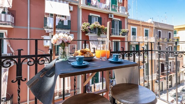 A balcony with a table set for breakfast, including croissants, juice, and flowers. - Street View Apartment by Rentbeat (Bari)