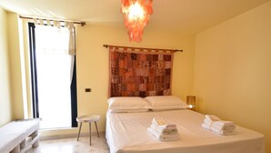 Una habitación de hotel con una cama, un taburete pequeño, un banco, una cortina estampada y una lámpara colgante.