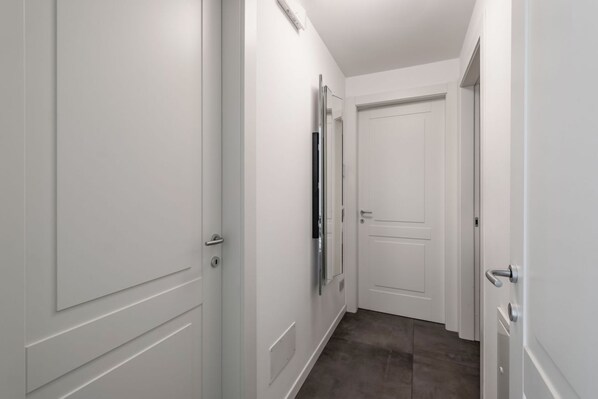 A narrow hallway with white walls and doors, a flat floor, and a door at the end.